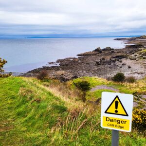 A photo displaying a "Danger Cliff Edge" sign and railing alongside a downward path.